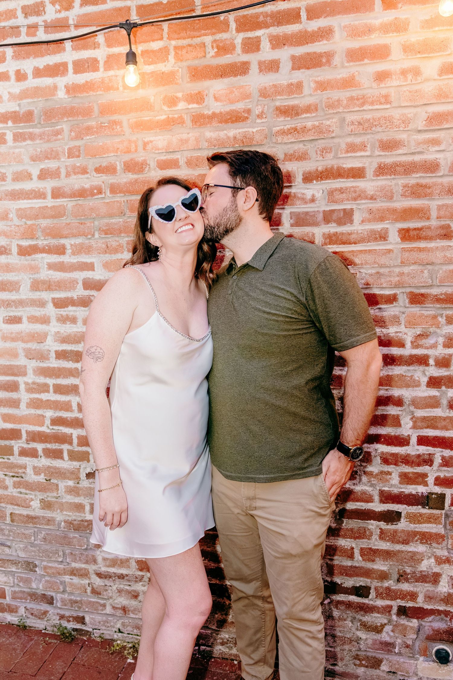 Bride and Groom posing against rustic brick wall, in a bar for their Wedding Welcome Dinner Party.