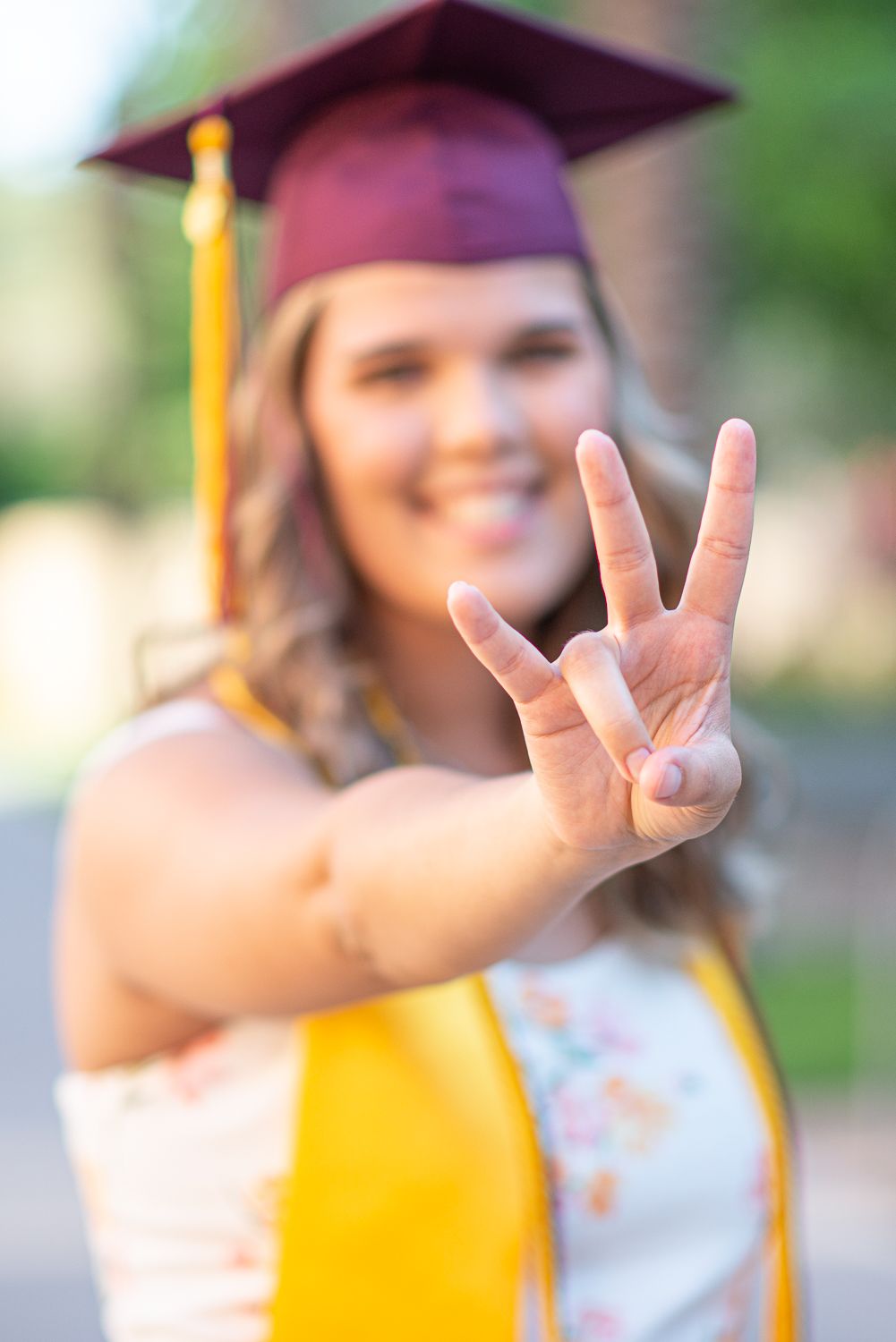 A graduate in cap and gown making peace sign gesture outdoors during graduation.