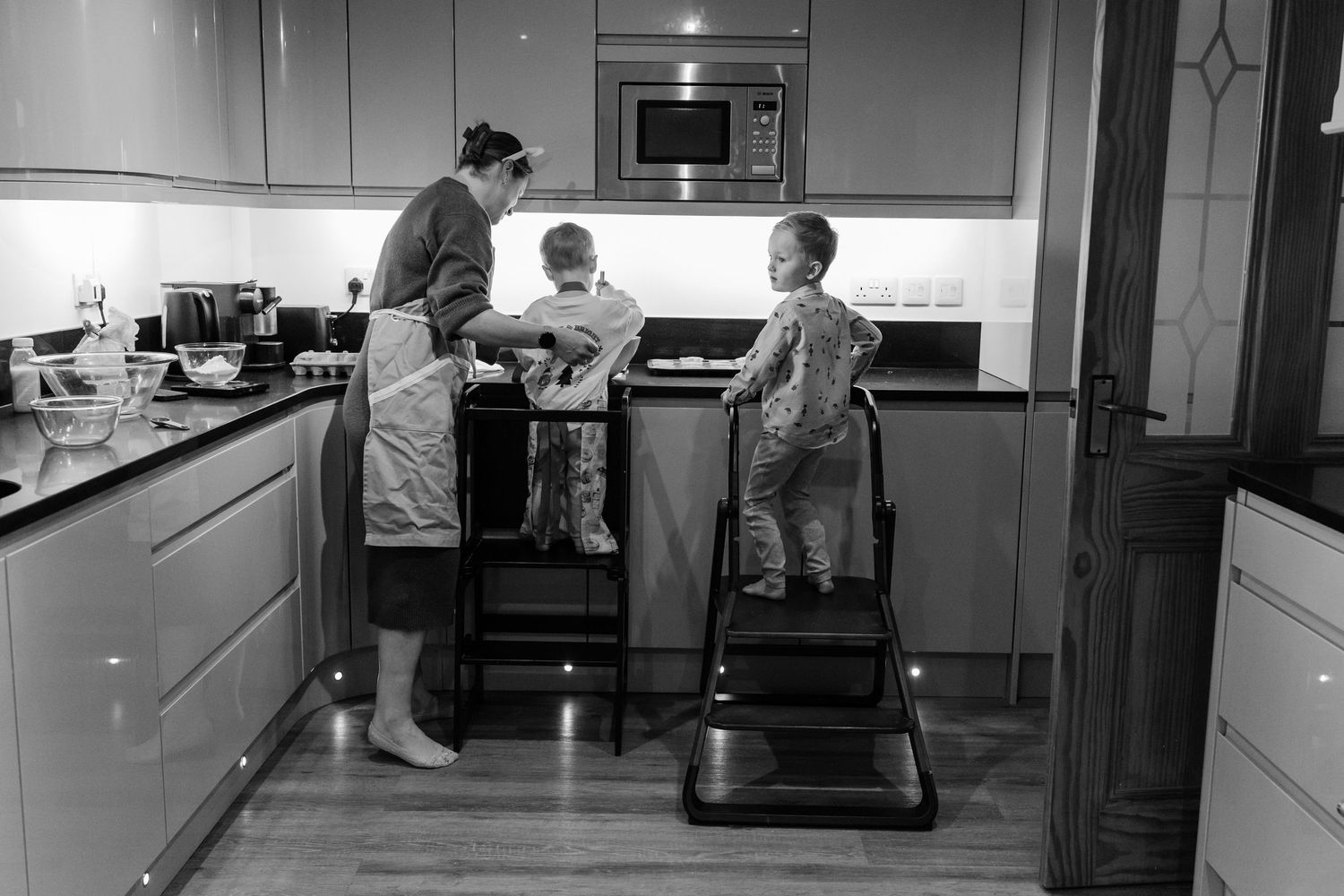 Black and white photo of a mother and two children cooking together in a modern kitchen.