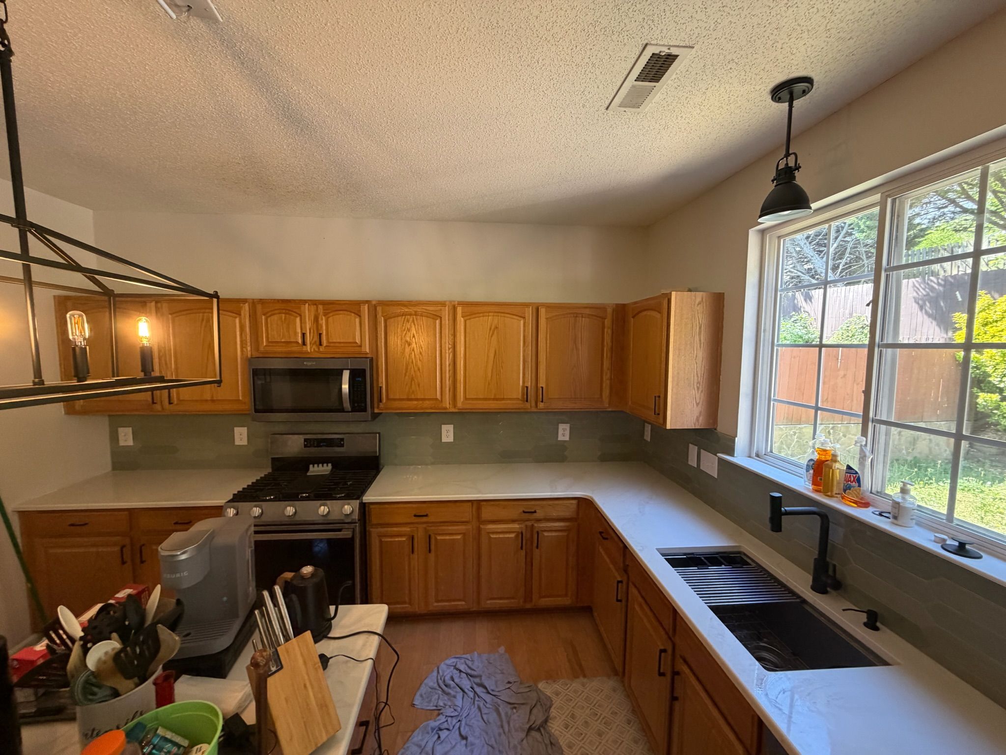 Oak kitchen cabinets with gray quartz countertops, stainless appliances, and green tile backsplash in bright kitchen.