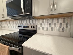 Modern kitchen with elongated hexagon marble mosaic backsplash tiles behind stainless steel microwave and range.