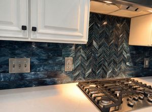 Dramatic deep blue herringbone mosaic tile kitchen backsplash with white cabinets and stainless steel gas cooktop.