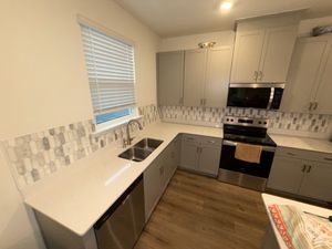Renovated kitchen featuring gray cabinets, quartz countertops, and geometric mosaic tile backsplash with stainless appliances.