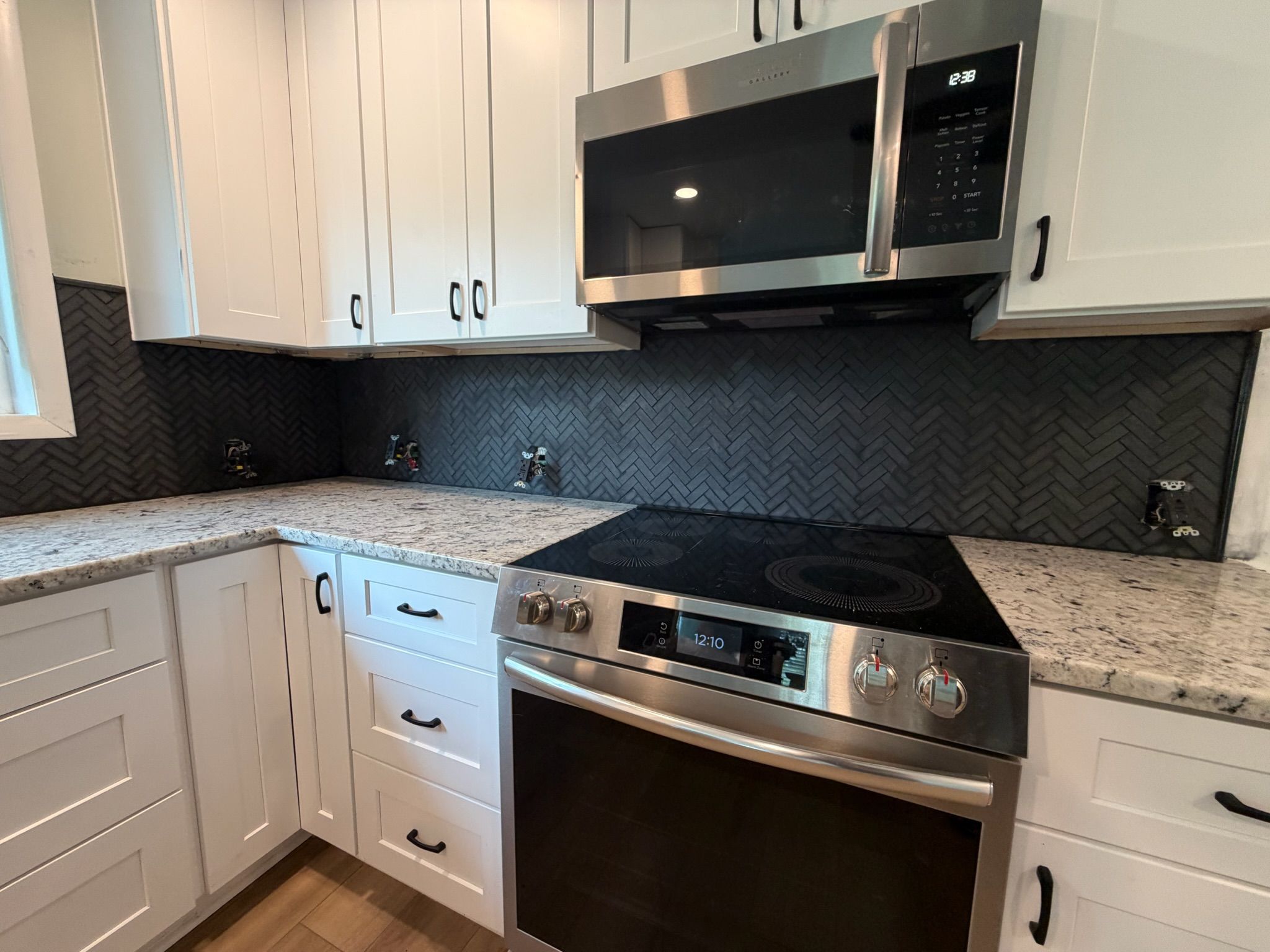Modern kitchen with white shaker cabinets, granite countertops, herringbone tile backsplash, and stainless steel appliances.