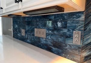 Bold blue herringbone glass tile kitchen backsplash with metallic switch plates beneath white cabinets.