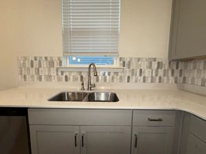 Gray cabinet kitchen with stainless double sink, mosaic stone tile backsplash, and white quartz countertop.
