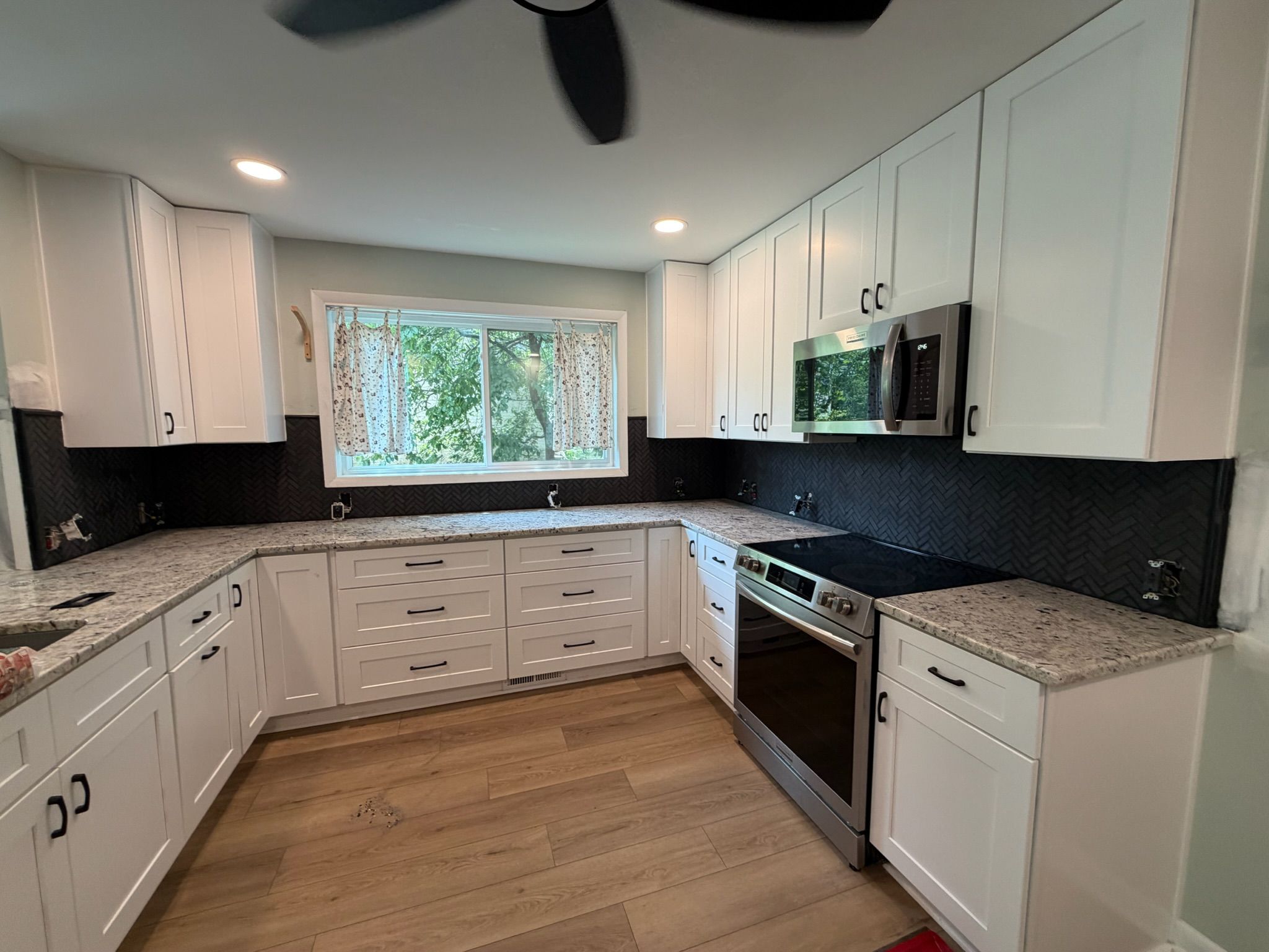 Modern kitchen with white shaker cabinets, dark backsplash, granite countertops, stainless steel appliances, and light hardwood floors.