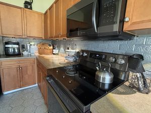 Oak kitchen cabinets with black appliances, decorative gray brick tile backsplash, and tan countertops.