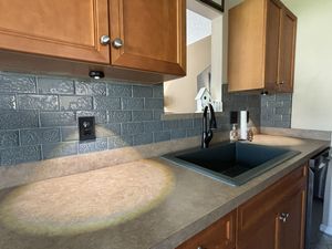 Oak kitchen cabinets with decorative gray embossed tile backsplash, black undermount sink, and tan countertops.