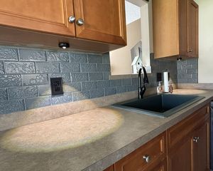 Oak kitchen cabinets with gray textured tile backsplash, undermount black sink, and tan countertops.