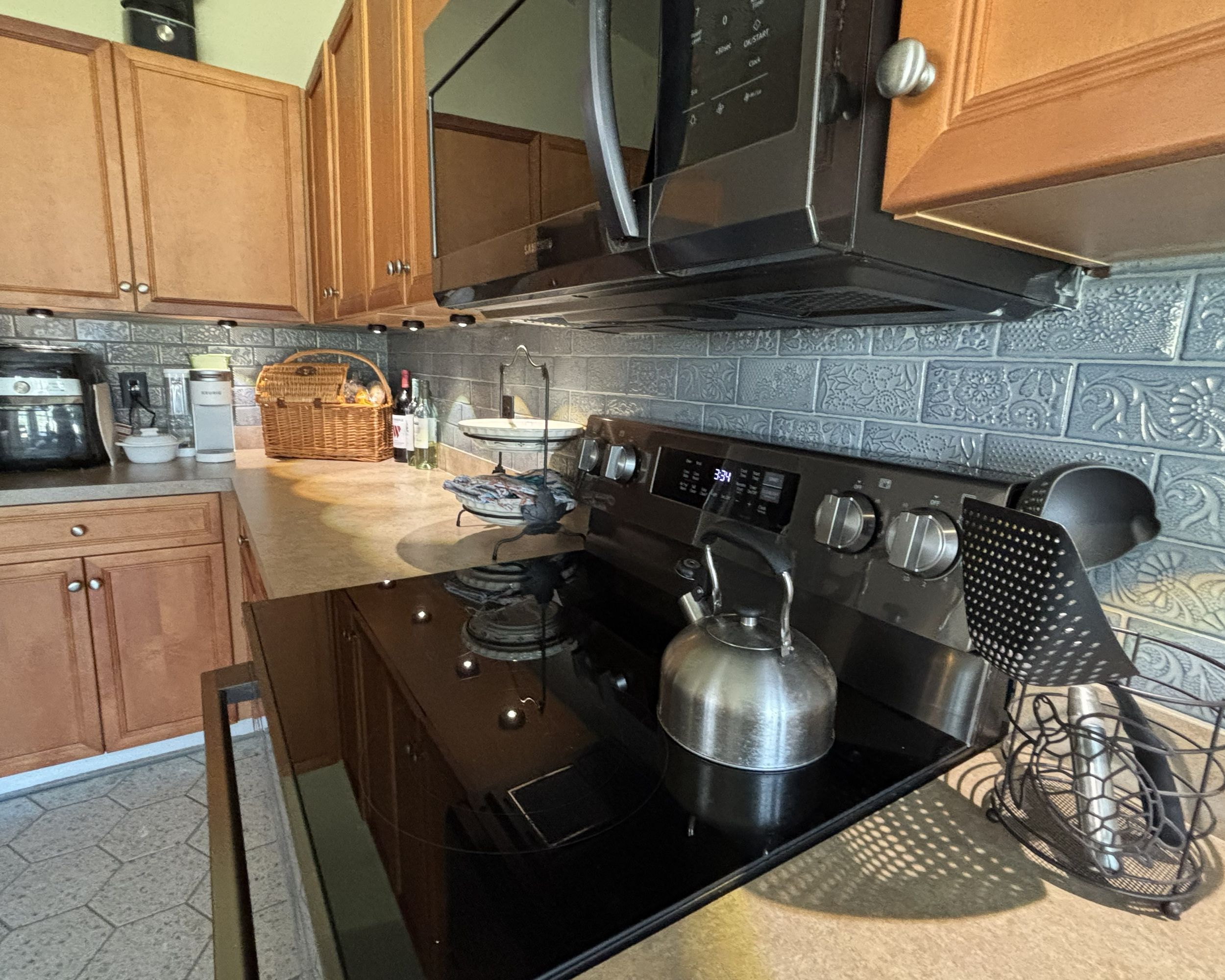 Oak kitchen with black electric range, over-range microwave, and decorative gray textured tile backsplash.
