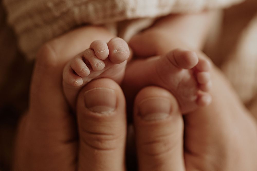 Close-up of tiny newborn baby feet cradled gently in adult hands, capturing a tender parent-child bonding moment.