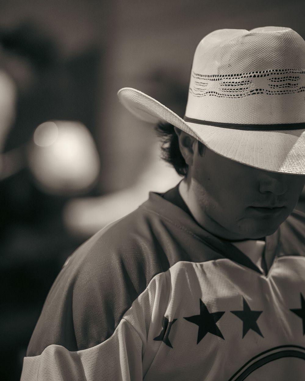 Black and white portrait of a cowboy in straw hat at a rodeo event.