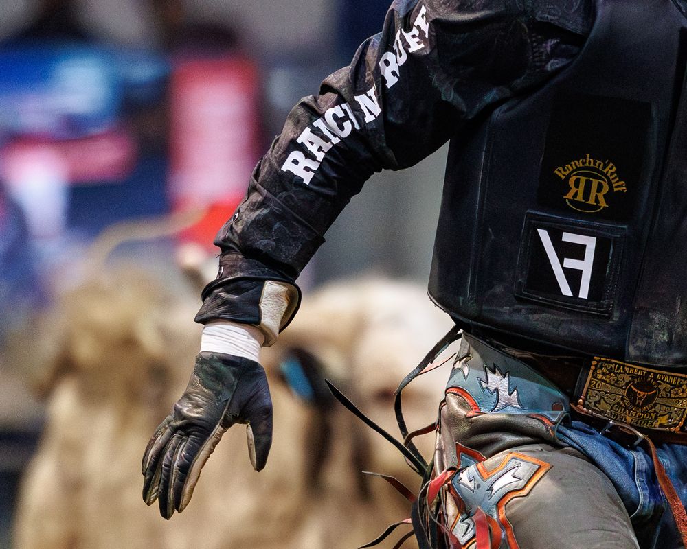 Close-up of a bull rider wearing Ranchin Sport gloves and gear during a rodeo competition.