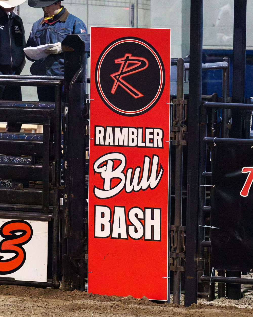 Red Rambler Bull Bash event signage displayed on arena fence at rodeo.