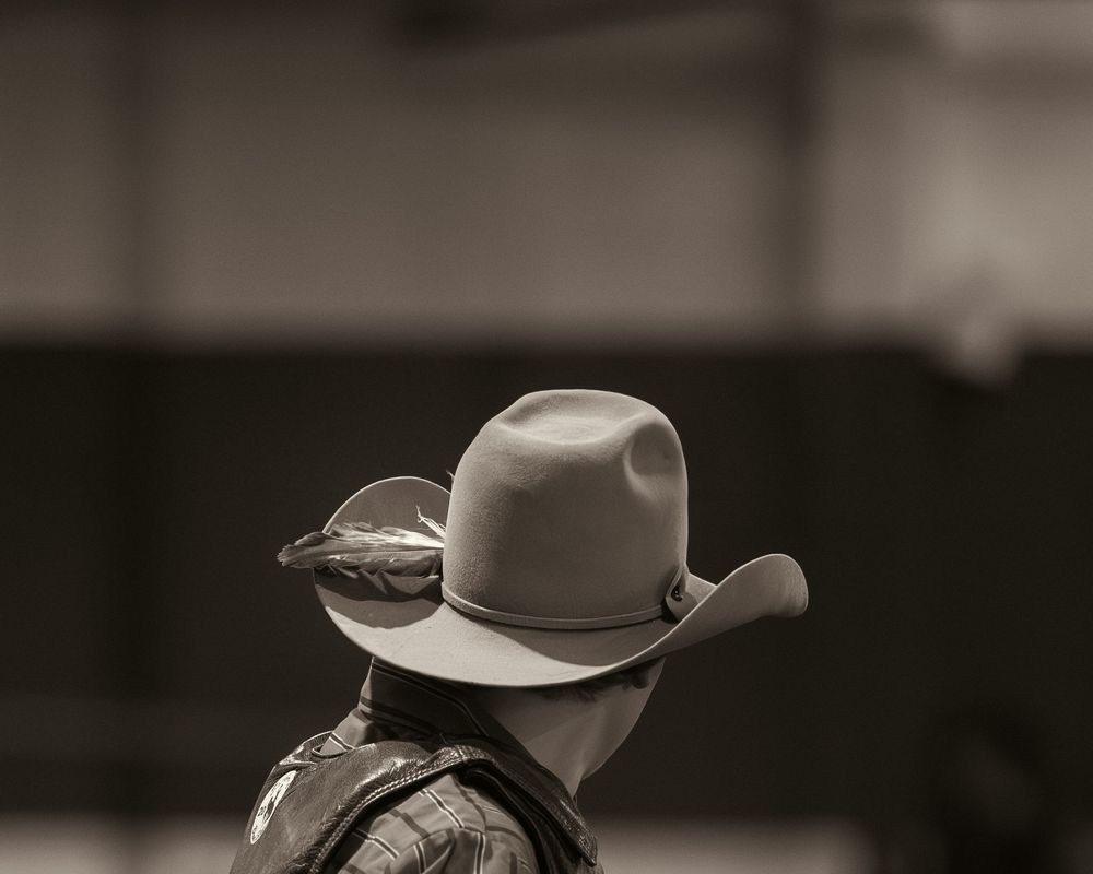 Black and white close-up portrait of cowboy wearing classic western hat with feather.