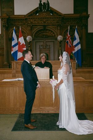 Bride and groom exchange vows before officiant in elegant wood-paneled courtroom with Canadian and Toronto flags.