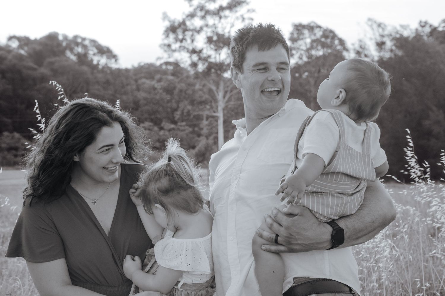 Black and white photo of a happy family with two young children laughing together with their parents in a sunny field in Rouse Hill.