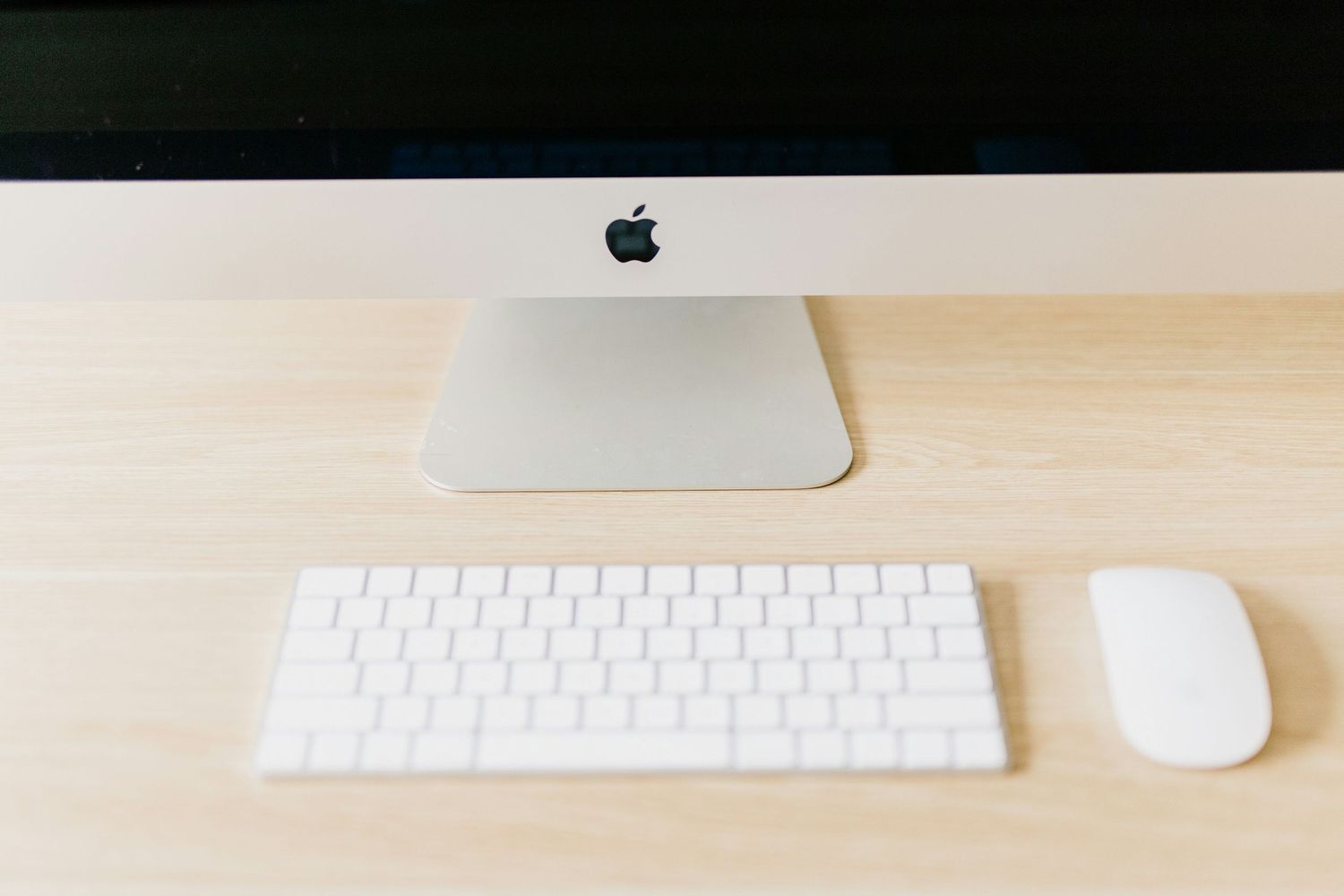 Apple iMac desktop computer with Magic Keyboard and Magic Mouse on a clean wooden desk surface.