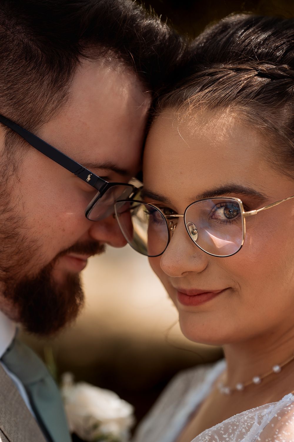 Close-up of a bride and groom in glasses touching foreheads tenderly on their wedding day.