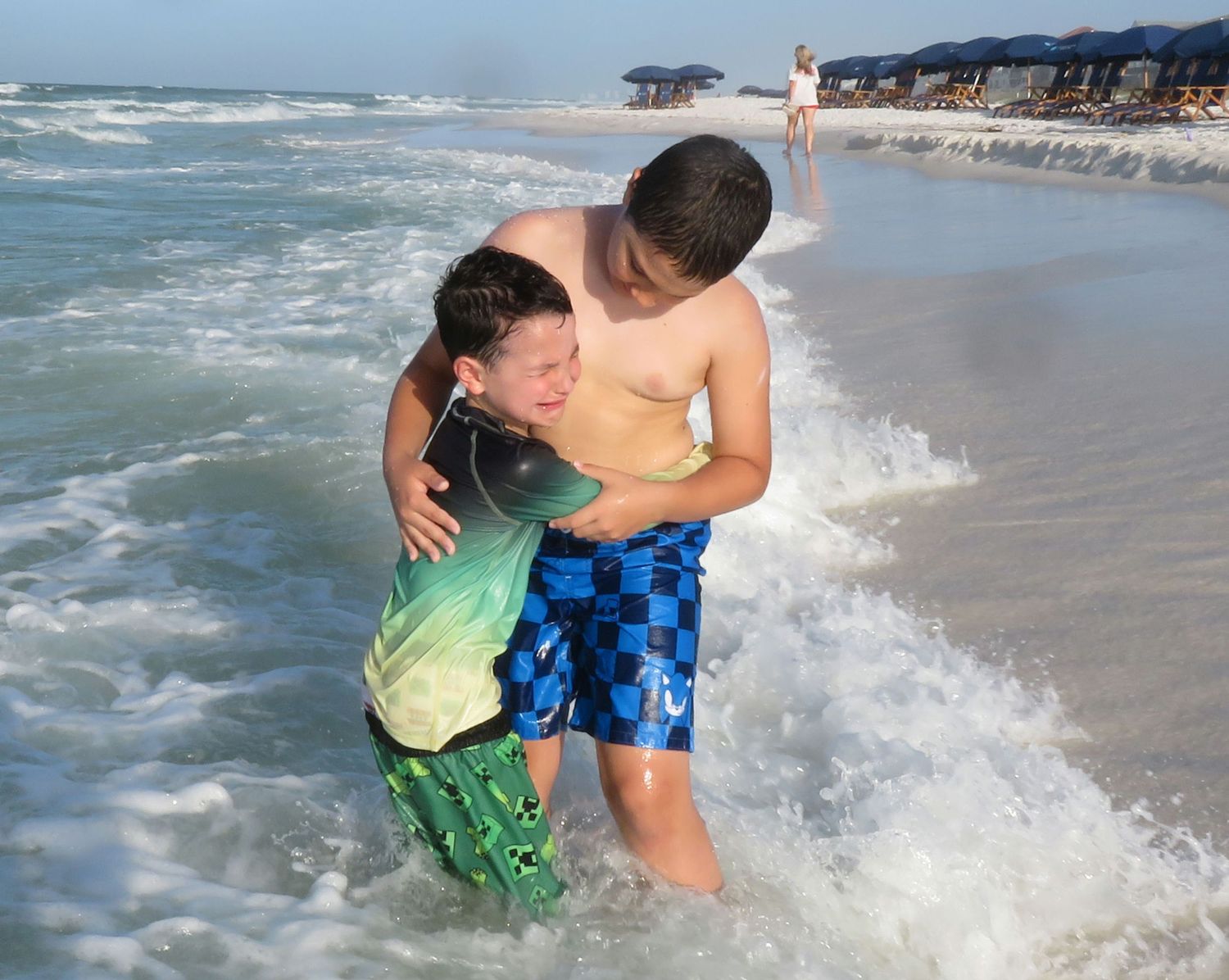 Older brother helping his younger brother after a wave during a family beach outing