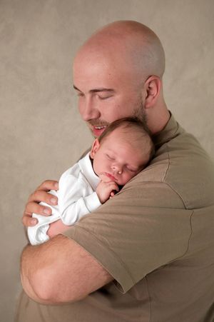 Bald father tenderly holding sleeping newborn baby against his chest in a warm embrace.