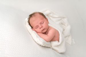 Peaceful newborn baby sleeping wrapped in a soft white blanket on a white background.