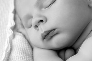 Close-up black and white portrait of a sleeping newborn baby with delicate features.