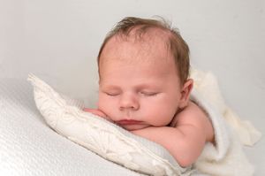 Peaceful newborn baby sleeping on a soft white pillow, wrapped in a cozy cream blanket.