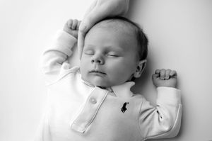 Black and white newborn baby sleeping peacefully in white Ralph Lauren onesie with tiny fists raised.