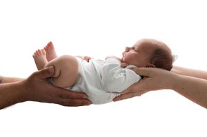Two hands gently cradling a sleeping newborn baby dressed in white against a white background.