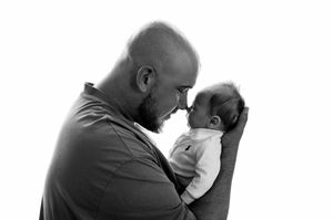 Black and white photo of a bald bearded man tenderly holding a newborn baby face-to-face in an intimate moment.