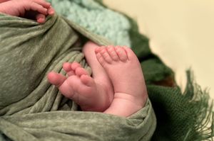 Close-up of newborn baby feet wrapped in a soft green swaddle blanket.