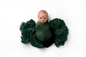 Newborn baby swaddled in dark green wrap cloth on white background.