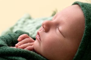 Close-up of peaceful sleeping newborn baby wearing green wrap and hat with tiny fingers near face.