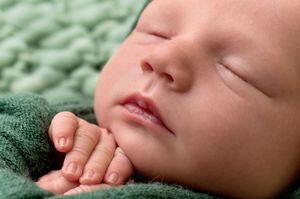 Peaceful newborn baby sleeping on a soft green knit blanket, close-up portrait of infant face and tiny hands.