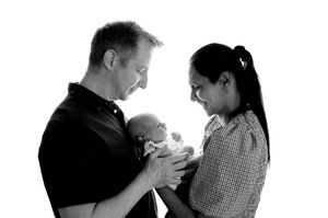 Black and white photo of parents smiling at their newborn baby held tenderly between them.