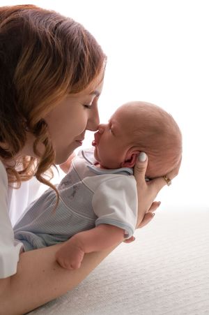 A tender moment as a redheaded mother touches noses with her newborn baby, cradling the infant gently in her hands.