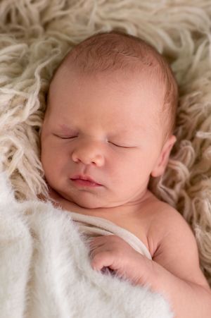 Peaceful newborn baby sleeping on a soft cream fluffy blanket, wrapped in white, perfect newborn photography.