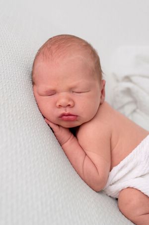 Peaceful newborn baby sleeping on white blanket, wrapped in soft white cloth, with delicate features and rosy skin.
