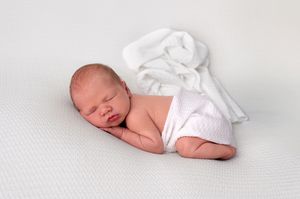 Peaceful newborn baby sleeping on white blanket in classic posed newborn photography portrait.