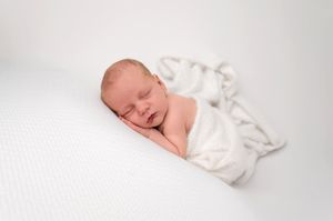 Peaceful newborn baby sleeping wrapped in a soft white blanket on a white background.