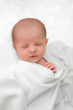 Peaceful newborn baby swaddled in white blanket sleeping on white background.