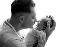 Black and white photo of a father tenderly kissing his newborn baby while cradling the infant in his hands.