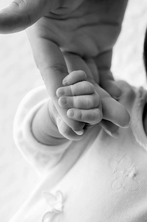 Black and white close-up of a newborn baby grasping an adult finger, symbolizing new life and parental bond.