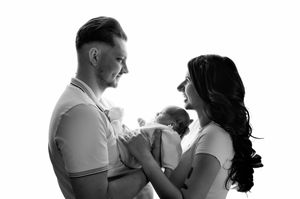Black and white photo of parents lovingly gazing at their newborn baby in a bright studio setting.