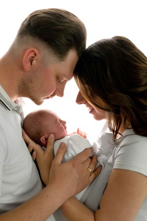 New parents tenderly touch foreheads while cradling their newborn baby together in a bright, intimate portrait.