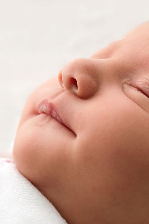 Close-up profile of a sleeping newborn baby with delicate features, soft skin, and tiny lips on a white background.