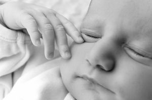 Close-up black and white photo of a sleeping newborn baby with tiny fingers resting gently on its face.