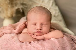 Peaceful newborn baby sleeping on pink wrap with hands under chin in professional photography studio portrait.